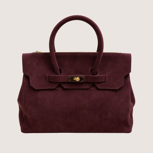 Deep burgundy suede handbag with a gold clasp on a light beige background.