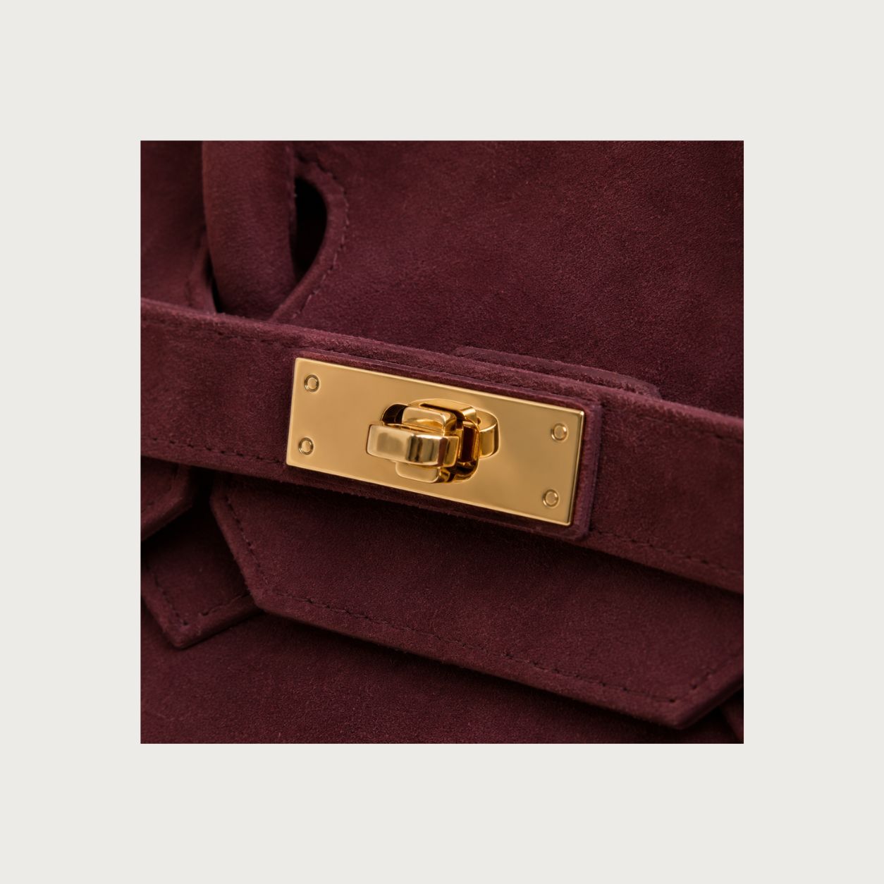 Close-up of polished gold hardware on deep burgundy suede handbag