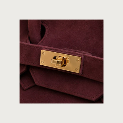Close-up of polished gold hardware on deep burgundy suede handbag