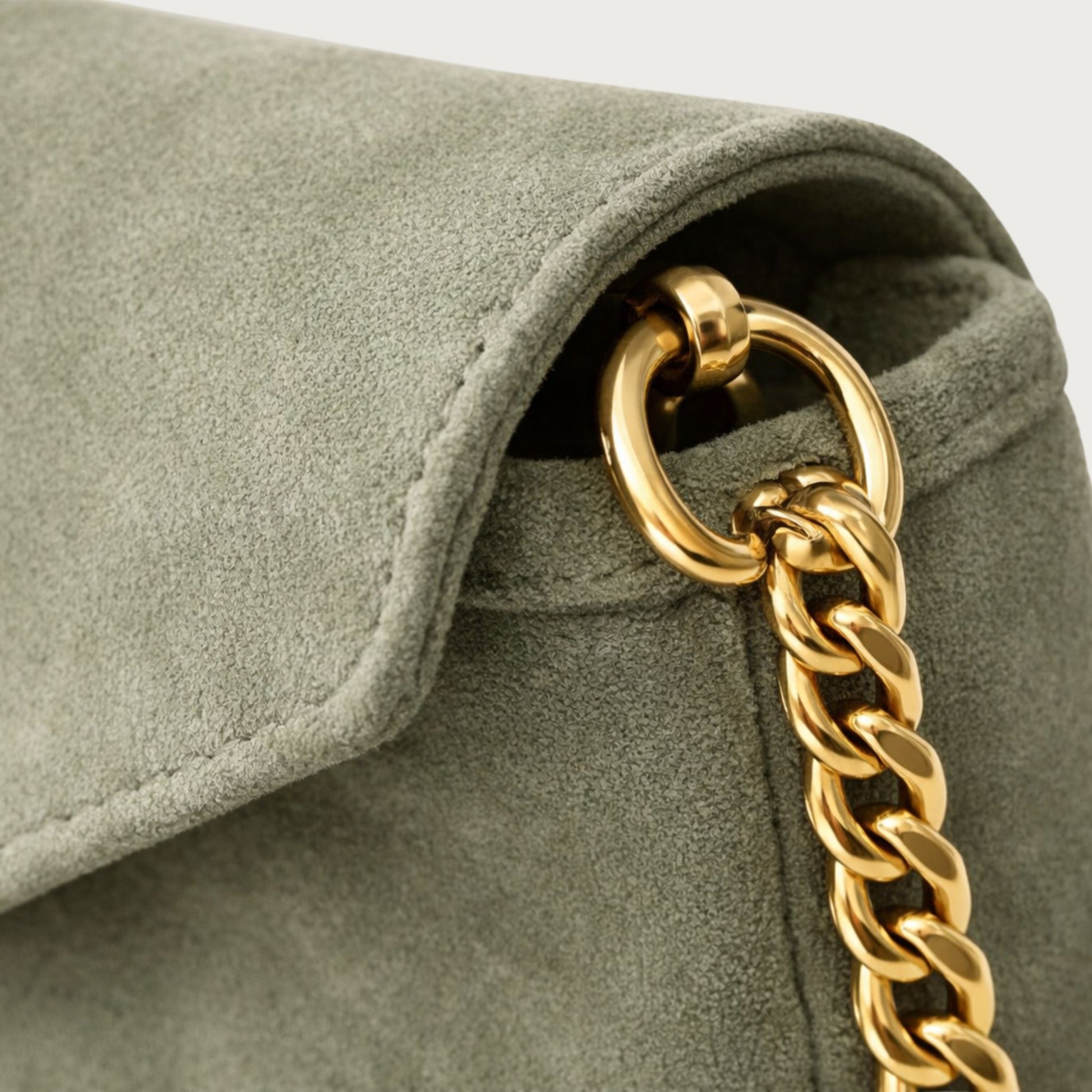 Close-up of the Nina convertible clutch showing the gold chain hardware and muted sage-green suede texture.