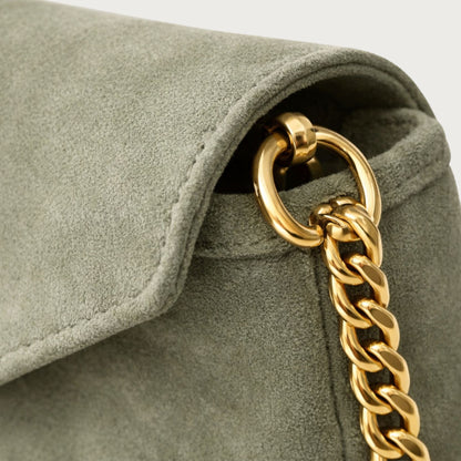 Close-up of the Nina convertible clutch showing the gold chain hardware and muted sage-green suede texture.